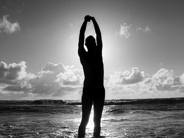 Silhouette of a man stretching against a sunrise.